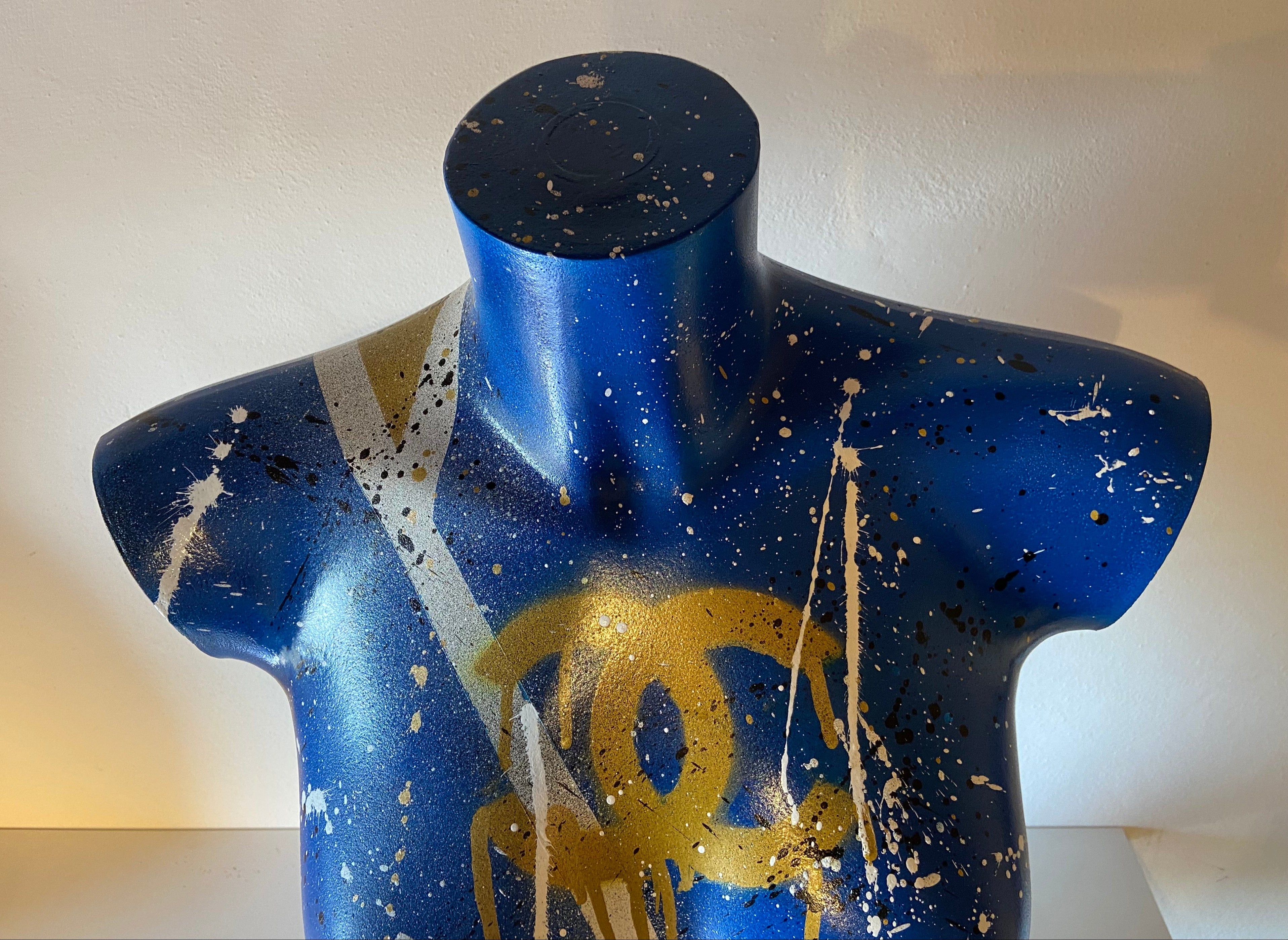 Scultura Lady Chanel, torso femminile blu cobalto con dettagli oro e spruzzi bianchi, opera pop art fashion.
